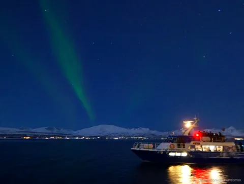 Zorza polarna nad fiordem widziana z łodzi podczas rejsu w Tromso